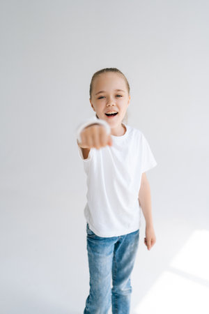 Vertical portrait of brave smiling little girl with broken hand wrapped in white plaster bandage playing gesturing with injured wrist on light isolated background. Concept of child healthcare.の写真素材