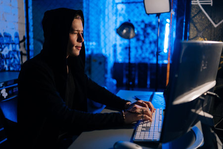 Side view of hidden hacker man wearing sweatshirt with hood engaged in hacking into security...