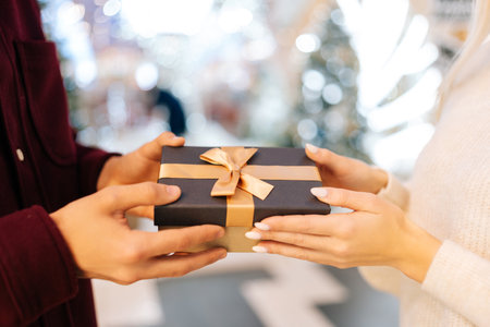 Close-up cropped shot of unrecognizable loving young man presenting gift box to happy woman in hall...