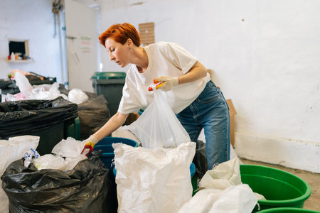 Side view of redhead female worker wearing latex gloves sorting diverse waste for further disposal...