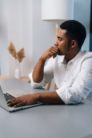 Vertical portrait of thoughtful black businessman working on business strategy on laptop sitting at...