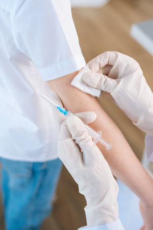 Vertical close-up cropped shot of unrecognizable female doctor applying plaster on shoulder of kid boy after vaccination injection. Concept of vaccination program, prevention of infectious diseases.の写真素材