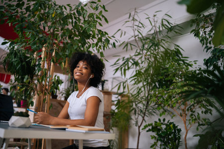 Low-angle portrait of pretty curly African American woman listening music in headphones sitting at...