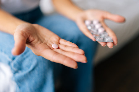 Close-up cropped shot of unrecognizable female patient holding pill in hand, taking medicine and...