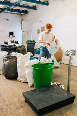 Vertical shot of concentrated female worker wearing latex gloves sorting diverse waste for further disposal at modern private waste recycling plant. Concept of recycling and garbage sorting.の写真素材