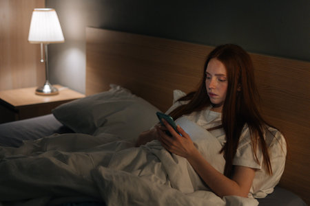 High-angle view of pretty young woman using smartphone, looking on screen, typing online message on...