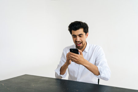 Studio portrait of enthusiastic excited young businessman in shirt celebrating success, looking at...