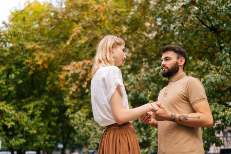 Shooting from below of pretty young couple in love standing at city park and looking at each other with falling in love eyes. Bearded handsome man and blonde woman walking spending time togetherの写真素材