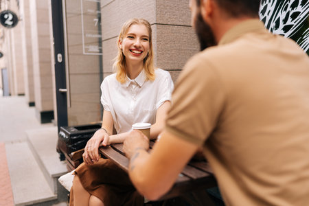 Pretty young dating couple having coffee together and enjoying life sitting at table in street cafe on summer day. View from back of unrecognizable man to laughing woman. Concept of urban lifestyle.の写真素材