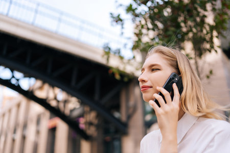 Close-up low-angle view of attractive blonde lady talking on mobile phone, holding smartphone close...