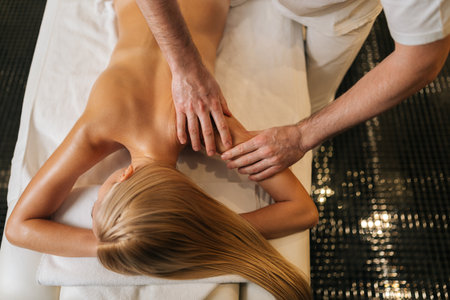 High-angle cropped shot view of professional male master doing back massage to female lying on treatment table in spa salon. Beautiful young woman lying on massage table, getting physiotherapy.の写真素材