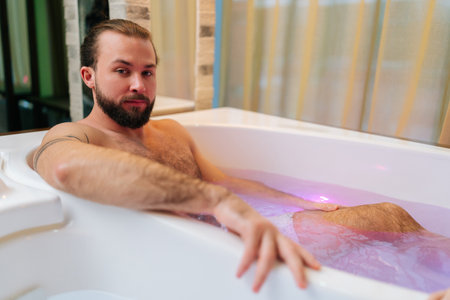 Portrait of handsome young man with beard lying in whirlpool enjoying hydromassage at luxury spa...