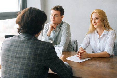 Positive professional young woman and man headhunters holding interview with unrecognizable male job seeker wearing suit. Two interested attentive hr managers listening to candidate on interview.の写真素材