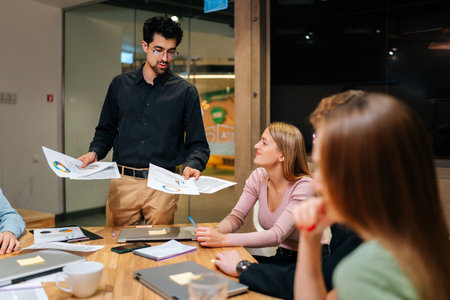 Positive multiethnic business team with male leader discussing project, brainstorming in office, talking, laughing. Corporate teacher training staff, mentoring employees, holding meeting training.の写真素材
