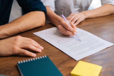 Close-up cropped shot of unrecognizable businesswoman sitting at table with pen in hands, ready signing profitable offer agreement after checking contract terms of conditions during deal meeting.の写真素材