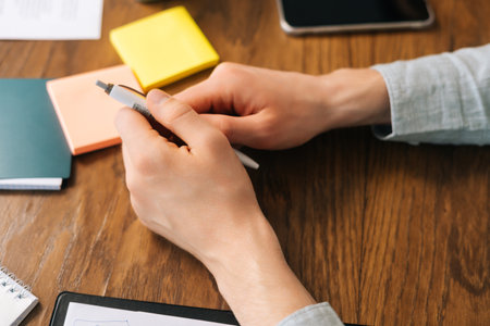 Close-up high-angle view hands of unrecognizable business man sitting at table and holding pen during deal meeting. Corporate decision making. Concept of corporate work meeting young startup teamの写真素材
