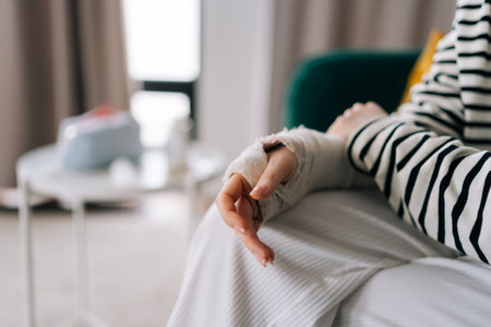 Detail cropped shot of suffering from pain unrecognizable young woman with broken hand wrapped in...