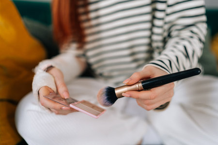 Closeup cropped shot of unrecognizable injured young woman with broken arm wrapped in white gypsum bandage applying cosmetic with makeup brush at home. Concept of insurance and healthcareの写真素材