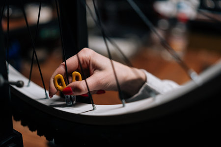 Close-up cropped shot of unrecognizable female cycling repairman hands checking bicycle wheel spoke with bike spoke key working in repair workshop with dark interior. Concept of bicycle maintenance.の写真素材