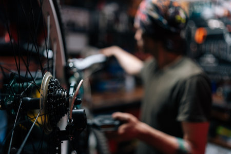 Closeup side view of unrecognizable blurred mechanic male repairing bike using special tool working in bicycle repair shop with dark interior. Concept of professional repair and maintenance of bike.の写真素材