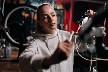 Closeup of serious blonde cycling mechanic female fixing bicycle handlebar with special tools working in bike repair shop with dark interior. Concept of professional maintenance of bicycle transport.の写真素材