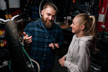 High-angle view of positive bearded cycling repairman communicating with smiling blonde female...