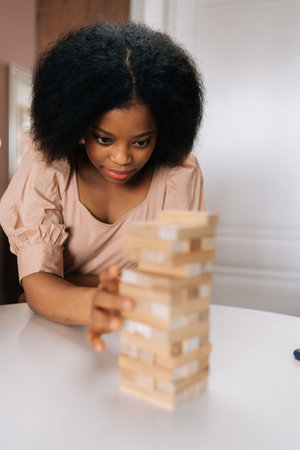 Closeup vertical portrait of serious African American woman playing tower block with diverse...