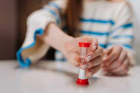 Close-up cropped shot of unrecognizable female hand holding hourglass while playing board games with...