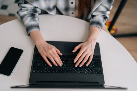 Closeup top view of unrecognizable female hands of business woman professional worker typing on laptop keyboard sitting at table, working on internet with computer software, programs, high angle view.の写真素材