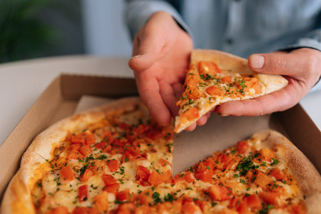 Close-up cropped shot of unrecognizable hungry mature male enjoying to eat pizza alone sitting at...