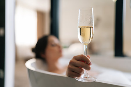 Closeup selective focus shot of young relaxed woman lying in foam bath holding glass champagne enjoying alcoholic drink during luxurious recreation for weekend. Brunette female relaxing in bathroom.の写真素材
