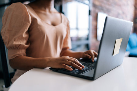 Close-up hands of unrecognizable African female student typing on notebook keyboard studying working online. Closeup of black businesswoman typing on laptop computer at desk from remote home office.の写真素材