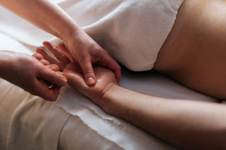 Close-up cropped shot of unrecognizable professional masseuse hands doing finger and palm massage to male client lying on massage table in spa salon. Woman physiotherapist doing relaxing massage man.の写真素材
