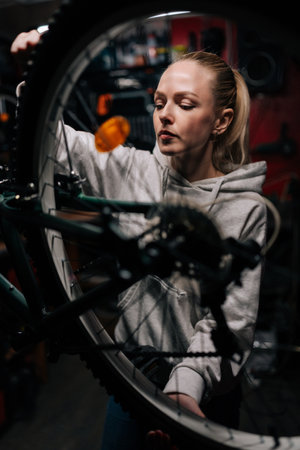 Vertical front view of blonde cycling mechanic female repairing and fixing mountain bicycle standing...