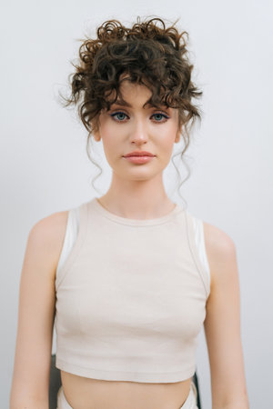 Vertical studio portrait of gorgeous young woman after applying professional makeup and making stylish hairstyle standing on isolated white background, looking at camera. Concept of fashion and beautyの写真素材