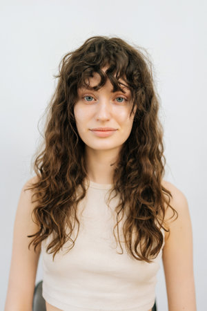 Vertical studio portrait of pretty young woman before applying professional makeup and making stylish hairstyle standing on isolated white background, looking at camera. Concept of fashion and beautyの写真素材