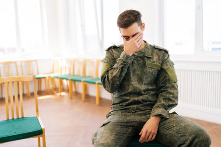 Portrait of bearded young Caucasian soldier in camouflage uniform with PTSD crying sitting in circle...