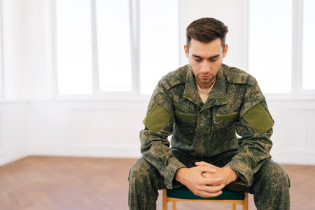 Portrait of frustrated veteran male in camouflage uniform sitting in circle during PTSD group therapy session looking down with pensive expression. Concept of mental health, psychotherapy.の写真素材