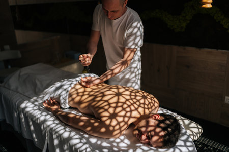 Professional manual therapist massaging man back with oil during relaxing or revitalizing procedure at Thai beauty spa salon. Guy client lying on couch enjoying body and skin care in wellness center..の写真素材