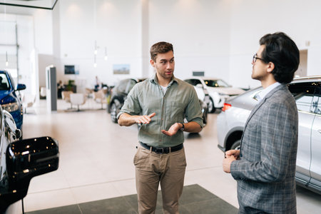Portrait of serious male client talking to professional car dealer in business suit in dealership discussing automobiles looking at luxurious new model. Concept of choosing and buying new auto.の写真素材