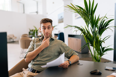 Portrait of shocked male client reading contract for real estate property purchase. Frustrated man reading terms of conditions of document, making decision about house purchase or financial investmentの写真素材