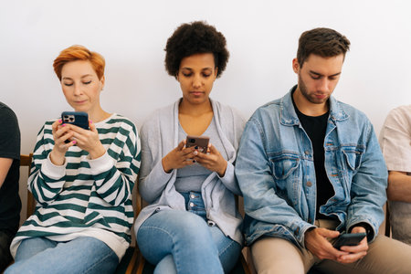 Cropped shot of bored multicultural and different ages people sitting in row using smartphones,...