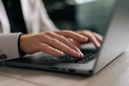 Close-up cropped shot of unrecognizable businessman in suit working on laptop computer by window....