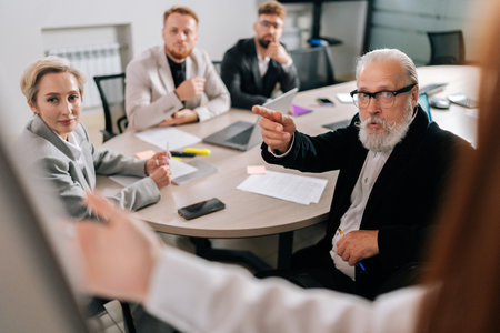 Back view of unrecognizable female manager presents new project plan to colleagues at meeting, explaining ideas on flipchart to coworkers in office. Businesswoman gives presentation, discussing ideas.の写真素材