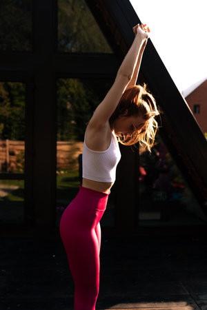 Vertical shot of sporty female wearing sportwear practicing warm up exercise, stretching arm,...