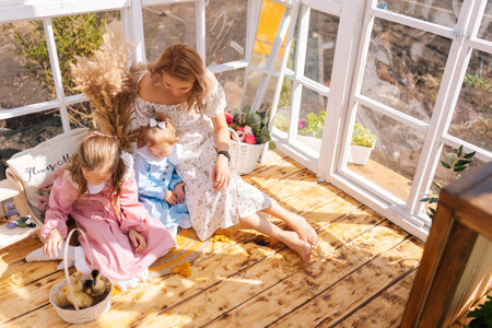 High-angle view of loving young mom and two adorable daughters in dress playing with little yellow...