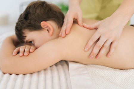 Closeup cropped shot of unrecognizable female masseur massaging back of five year old boy in spa salon. Close up of therapeutic, preventive massage session using oil, relaxing muscles.の写真素材