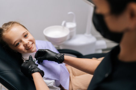 Portrait of cute child girl preparation for examination and treatment of oral cavity, orthodontics and pediatric dentist. Close-up of unrecognizable dentist puts napkin on girl looking at camera.の写真素材