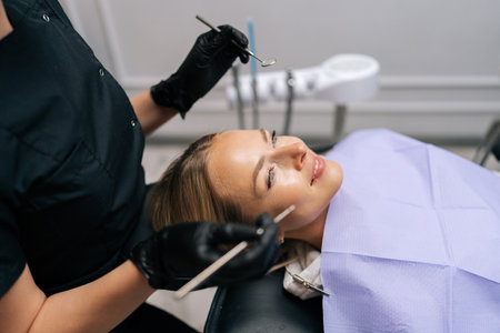 Closeup side view of unrecognizable female dentist in gloves examining teeth of smiling young woman using dental equipment instrument in dentistry clinic. Concept of modern teeth treatment.の写真素材