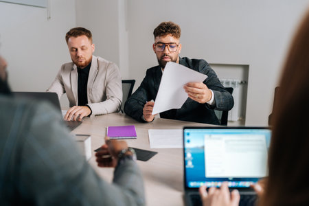 Serious young businessman reading contract document thinking considering risks with professional...